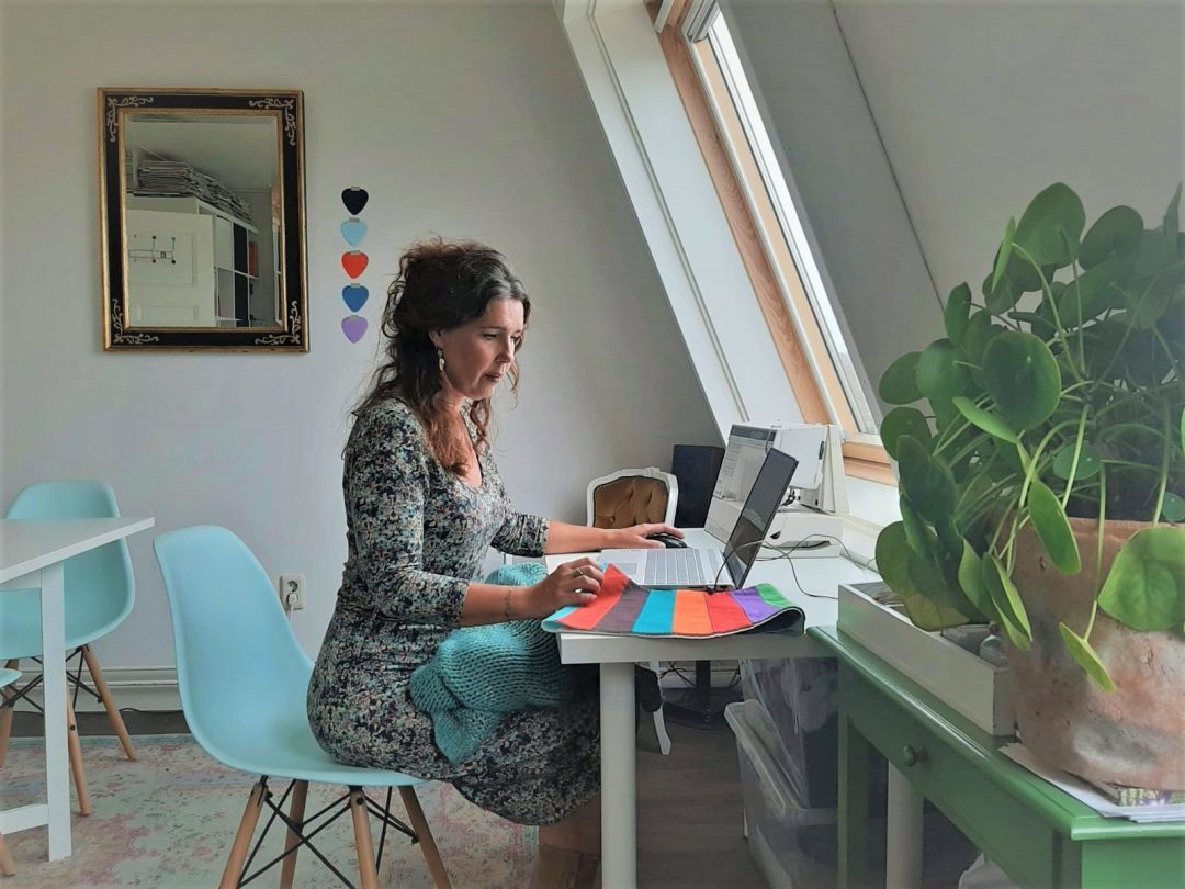 Ebrina aan haar bureau in de studio in Zwolle, met kleurdoeken naast de laptop